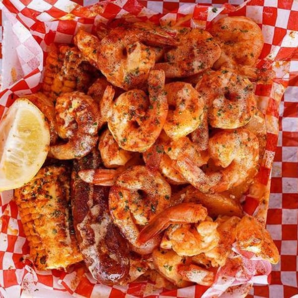 Cajun seasoned shrimp, corn on the cob, and sausage in a red and white checkered basket.