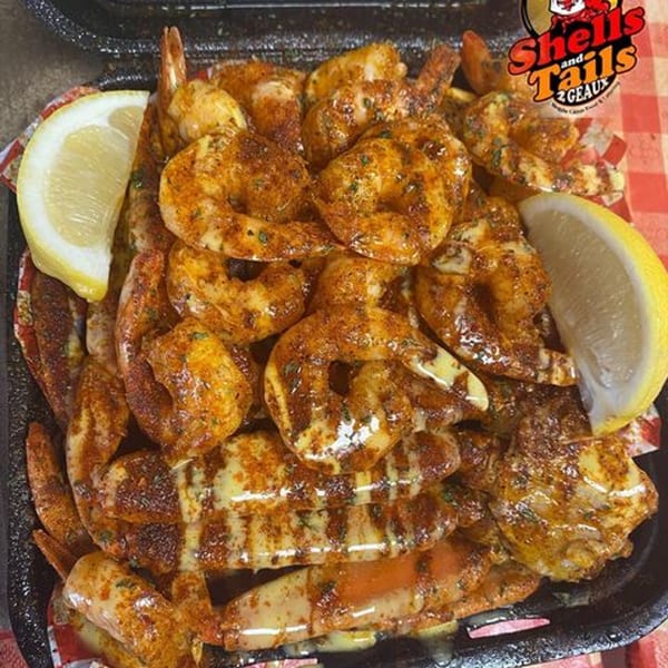 Cajun seasoned shrimp with lemon wedges in a black container on a red and white checkered tablecloth.