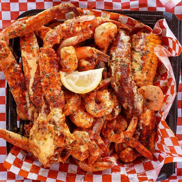 Cajun seafood boil with crab legs, shrimp, corn on the cob, and a lemon wedge in a black tray.