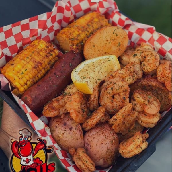 Cajun shrimp boil with corn, sausage, potatoes, and a lemon wedge in a red and white checkered basket.