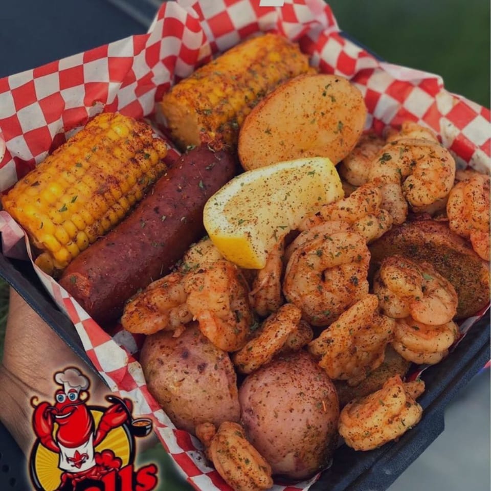 Cajun shrimp boil with corn, sausage, potatoes, and a lemon wedge in a red and white checkered basket.